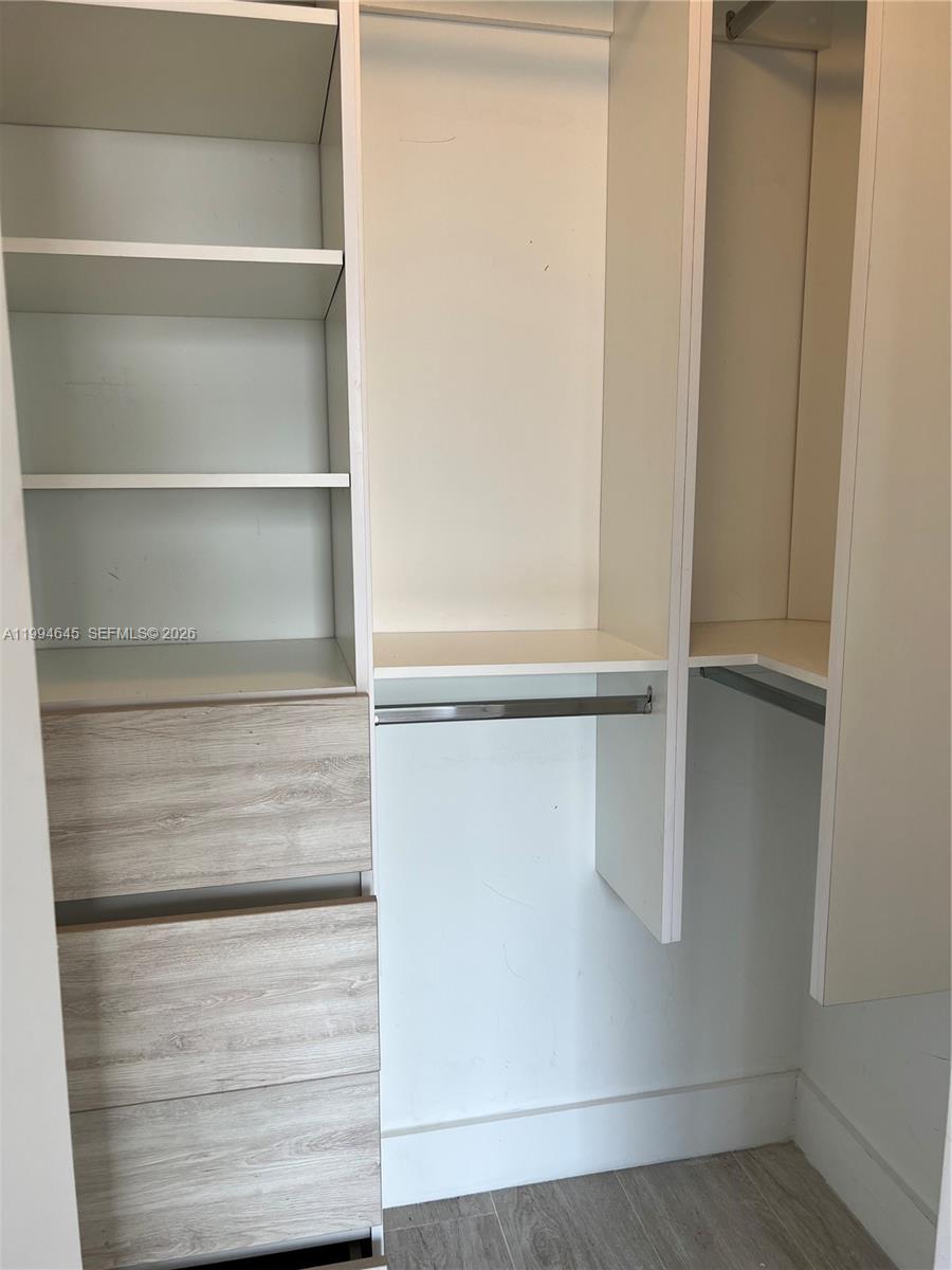 A walk-in closet features white shelving, hanging rods, and light wood-grain drawers — 121 NE 34th St # 1207, Miami FL 33137, MIAMI, FL