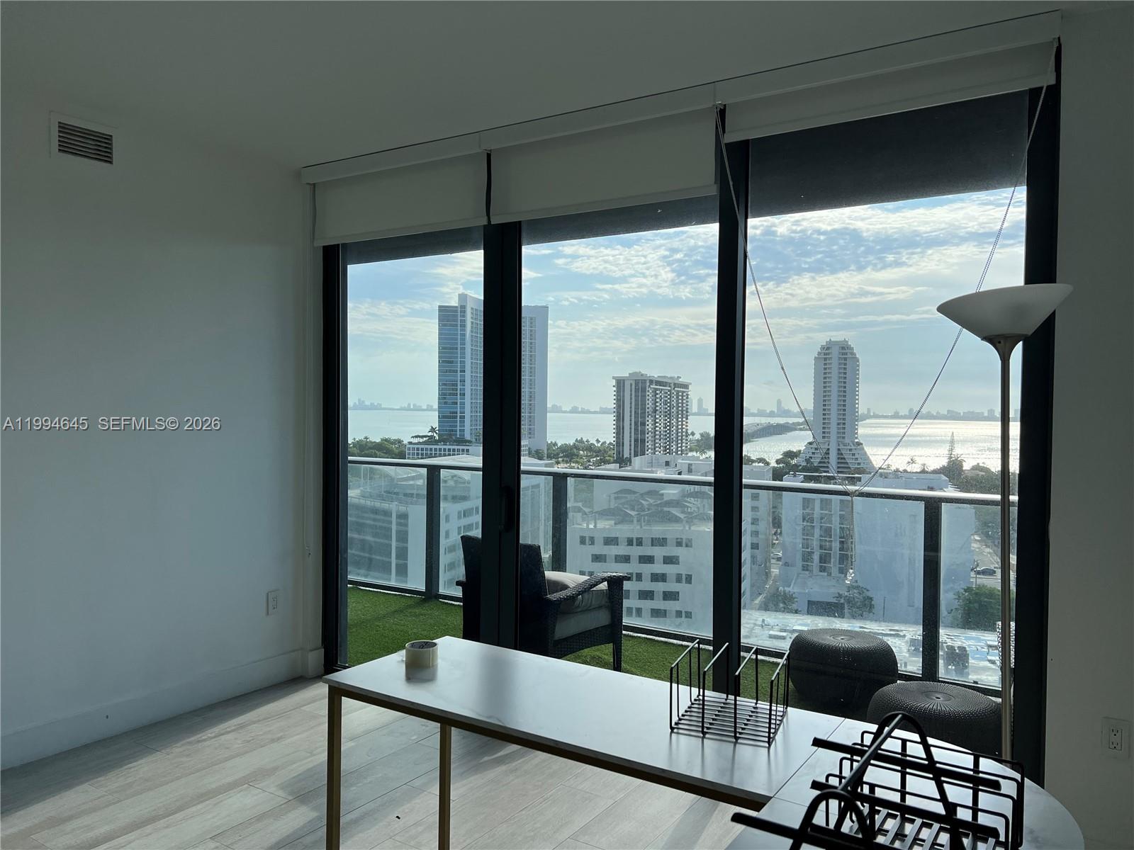 A room with light wood floors, a desk, and a balcony overlooking a city skyline — 121 NE 34th St # 1207, Miami FL 33137, MIAMI, FL