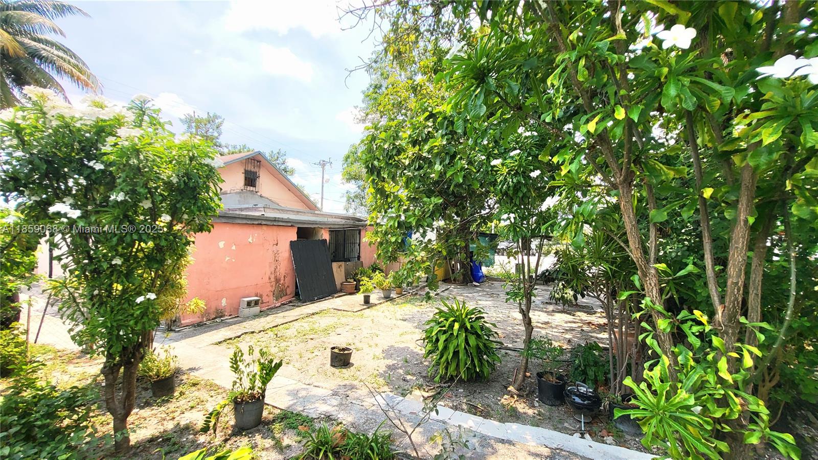 A pink house exterior is surrounded by trees and potted plants in a yard — 683 NW 30th St, Miami FL 33127, MIAMI, FL
