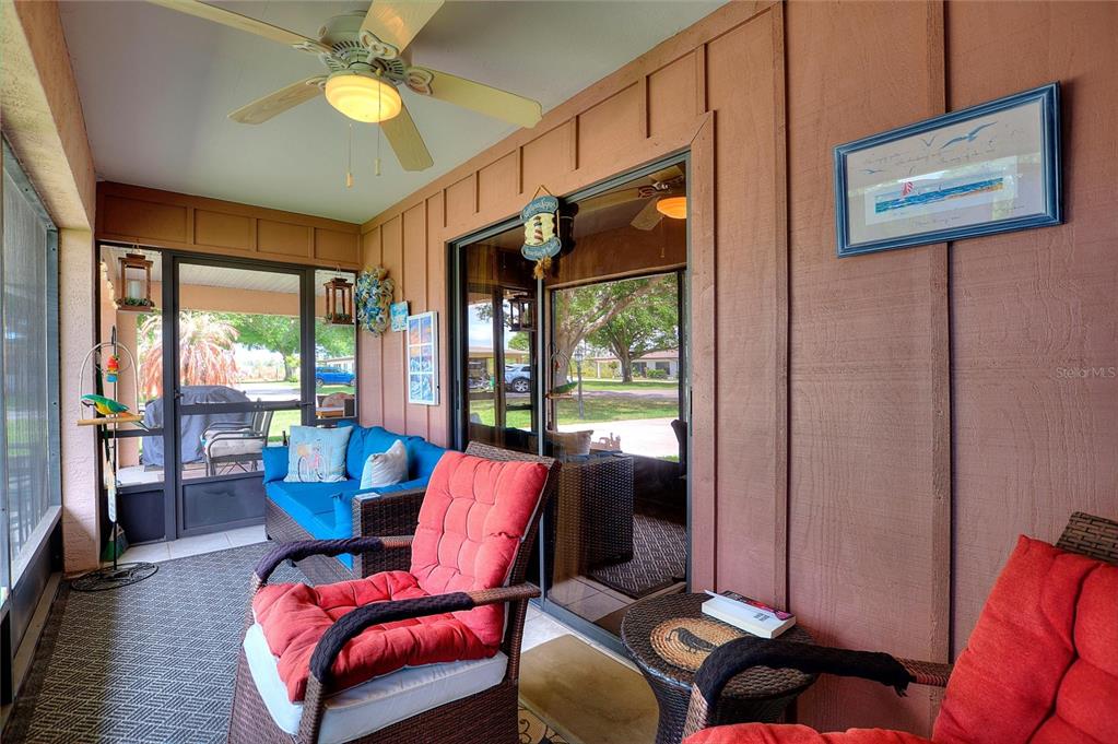A screened-in porch features wood-paneled walls, wicker furniture with red cushions, and a ceiling fan — 302 GENESIS POINTE DRIVE, LAKE WALES, FL