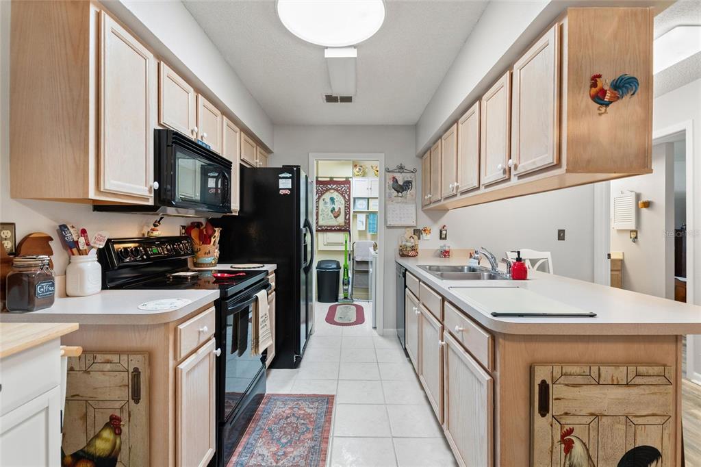 A galley kitchen features light wood cabinets, black appliances, and white countertops — 302 GENESIS POINTE DRIVE, LAKE WALES, FL