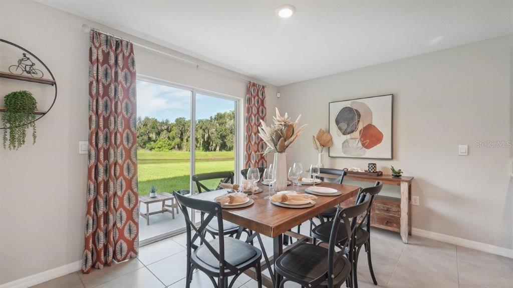 A dining room features a wooden table, black chairs, patterned curtains, and a sliding glass door — 17563 ACORN DROP ROAD, LAND O LAKES, FL