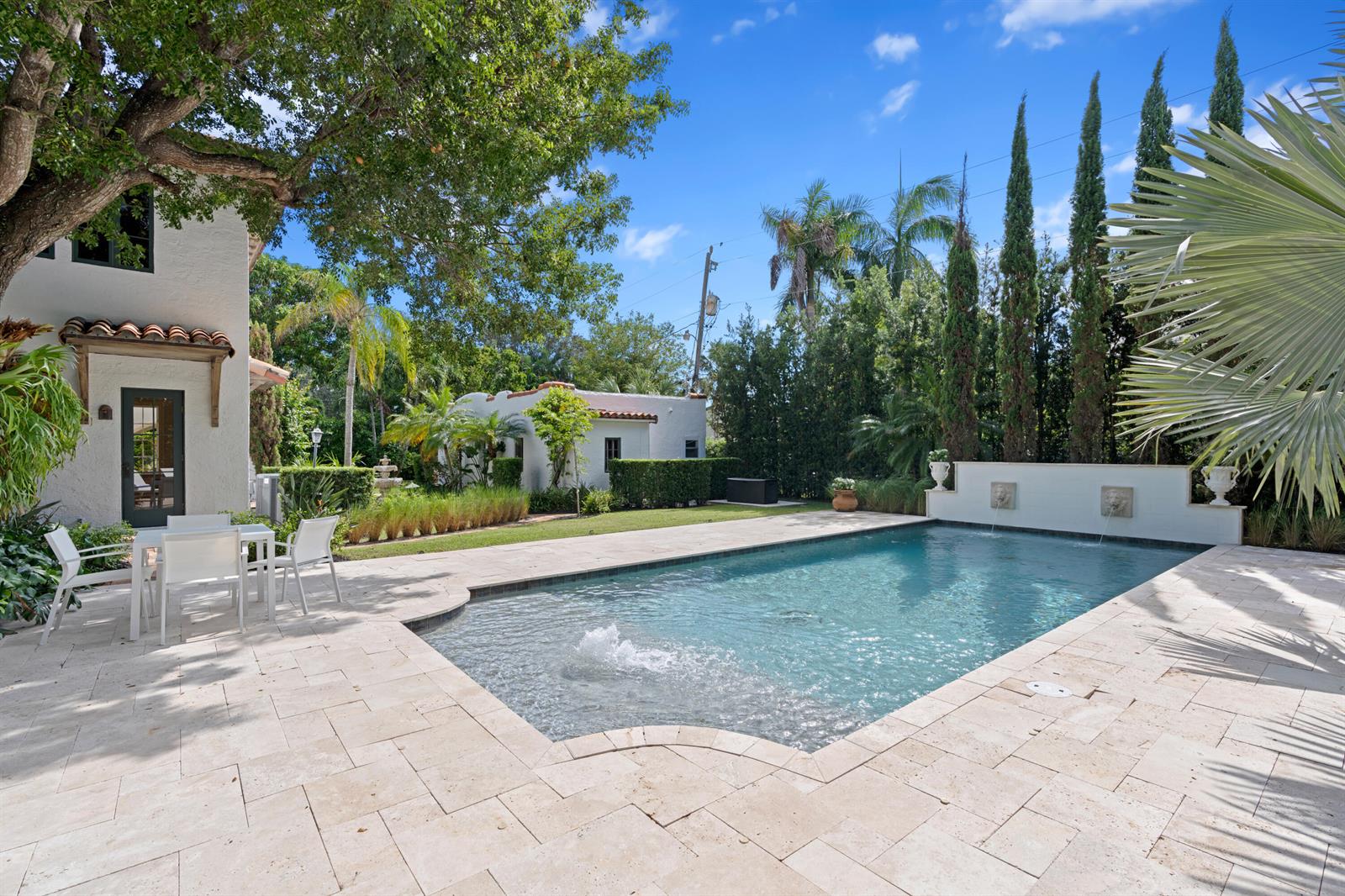A swimming pool with a fountain sits on a stone patio beside a white house — 308 BARCELONA Road, West Palm Beach FL 33401, WEST PALM BEACH, FL