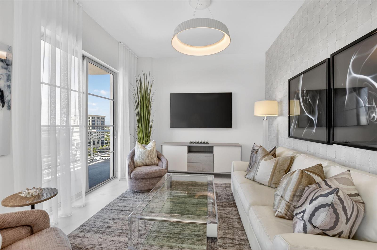 A modern living room features a white sofa, glass coffee table, wall-mounted television, and balcony — 155 E Boca Raton Road # 1201, Boca Raton FL 33432, BOCA RATON, FL