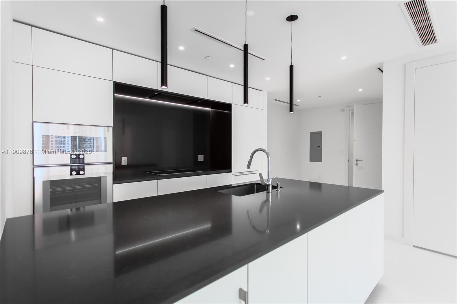 A modern kitchen features white cabinetry, a black island countertop, and three hanging pendant lights — 300 Biscayne Blvd Way # 1003, Miami FL 33131, MIAMI, FL