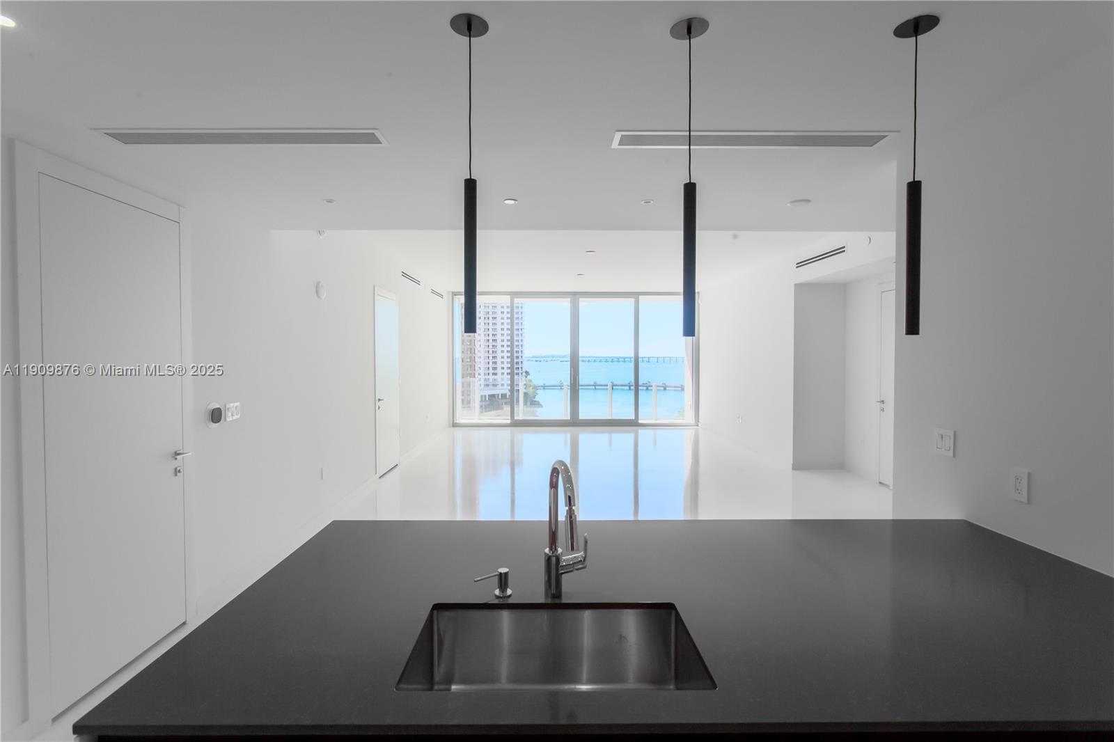 A kitchen island with a stainless steel sink overlooks a bright, minimalist living area — 300 Biscayne Blvd Way # 1003, Miami FL 33131, MIAMI, FL