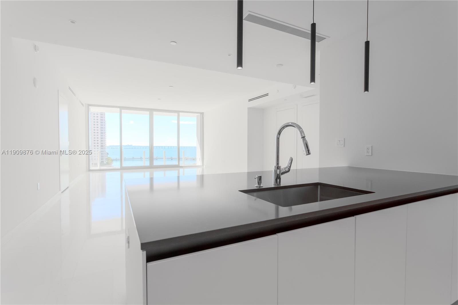 A modern kitchen island with a dark countertop faces a bright living area with water views — 300 Biscayne Blvd Way # 1003, Miami FL 33131, MIAMI, FL