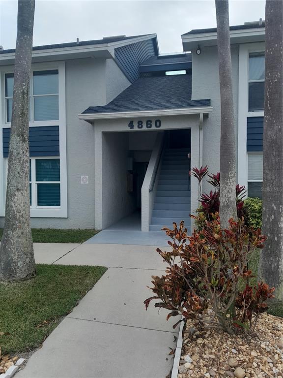 The exterior of a two-story apartment building features a covered entrance with stairs and landscaping — 4860 S ATLANTIC AVENUE UNIT 201, NEW SMYRNA BEACH, FL