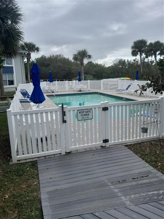 A white fenced swimming pool area features blue umbrellas and lounge chairs on a patio — 4860 S ATLANTIC AVENUE UNIT 201, NEW SMYRNA BEACH, FL
