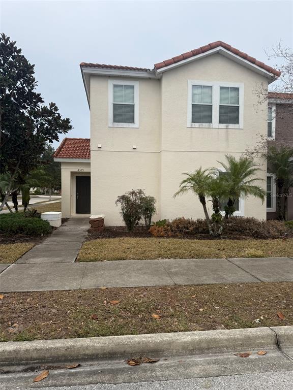 A two-story beige stucco house with a red tile roof and a front walkway — 4573 ADA LANE, KISSIMMEE, FL
