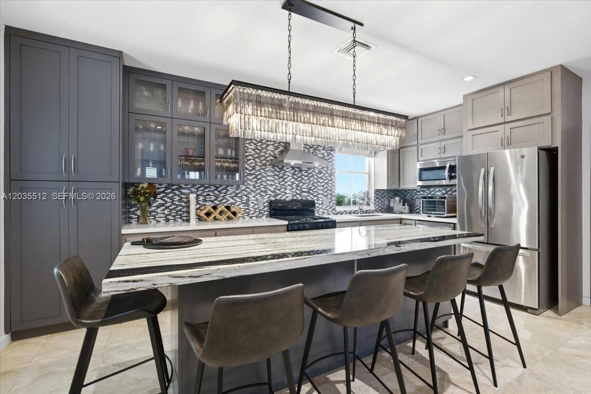 A modern kitchen features a large marble-topped island, gray cabinetry, and a crystal chandelier — 2917 Jackson Ave, Miami FL 33133, MIAMI, FL