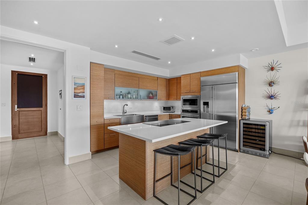 A modern kitchen features wood cabinets, a white island with bar stools, and stainless appliances — 7000 BAHIA BEACH DR UNIT 7258, RIO GRANDE, PR