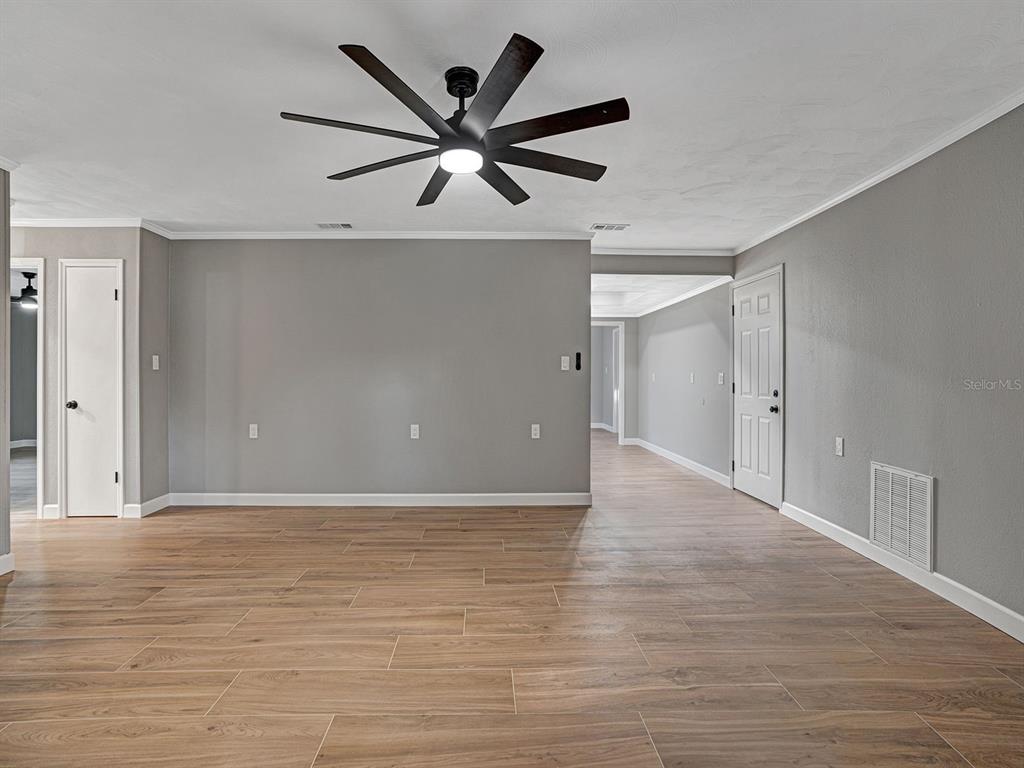 A spacious room with gray walls, wood-look tile flooring, and a large ceiling fan — 8310 LIMAN DRIVE, NEW PORT RICHEY, FL