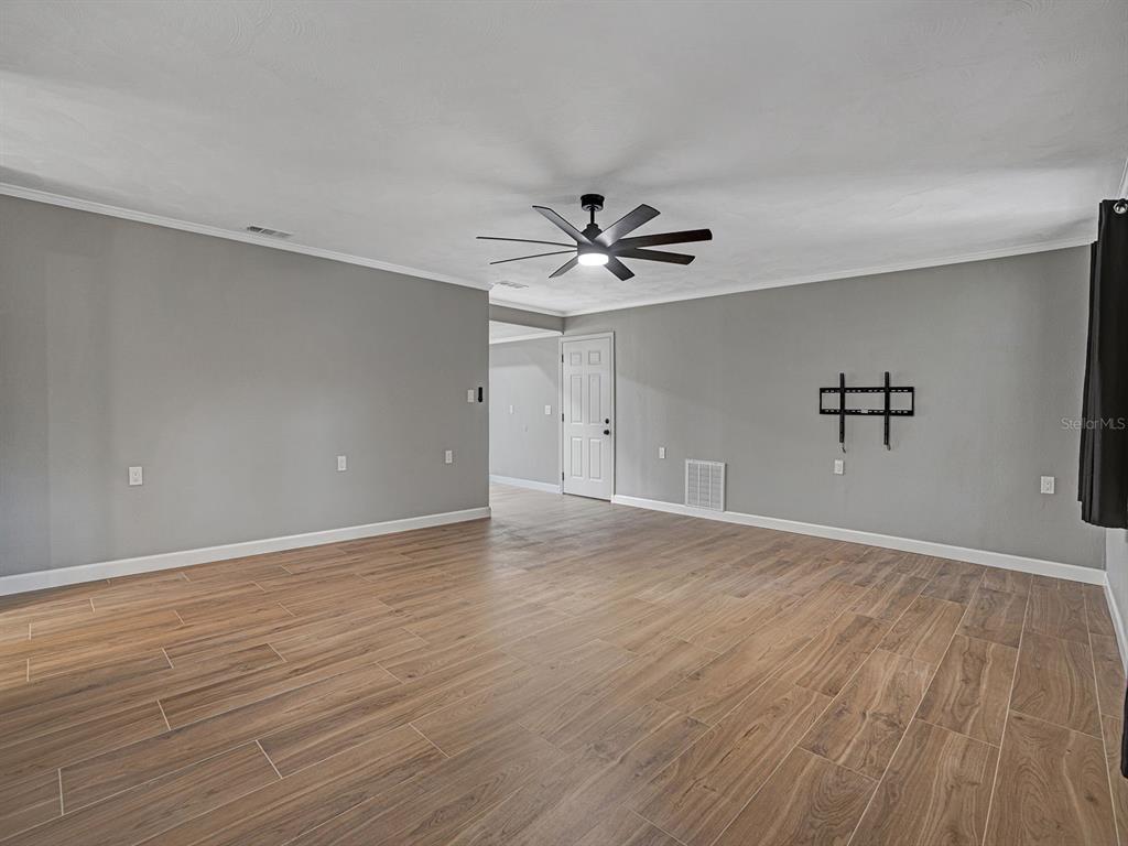 A living room features gray walls, wood-look tile flooring, a ceiling fan, and a wall-mounted bracket — 8310 LIMAN DRIVE, NEW PORT RICHEY, FL
