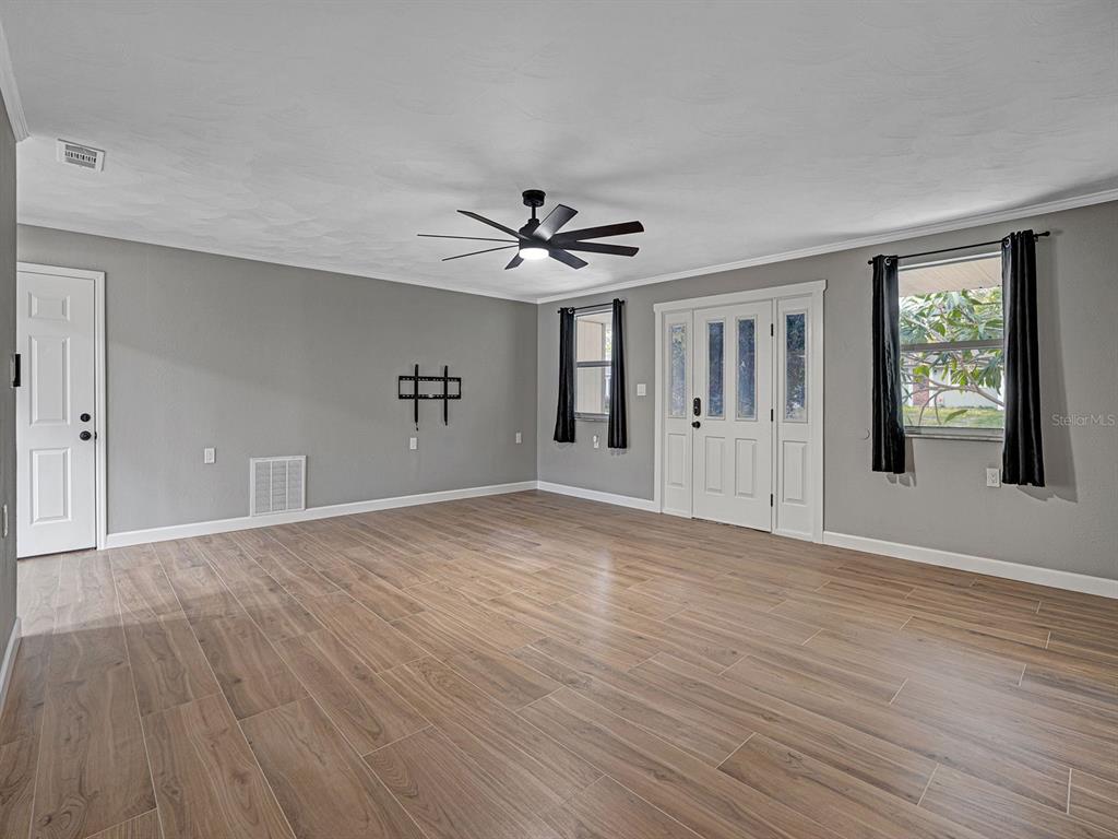 A living room features gray walls, wood-look tile flooring, a ceiling fan, and a front door — 8310 LIMAN DRIVE, NEW PORT RICHEY, FL