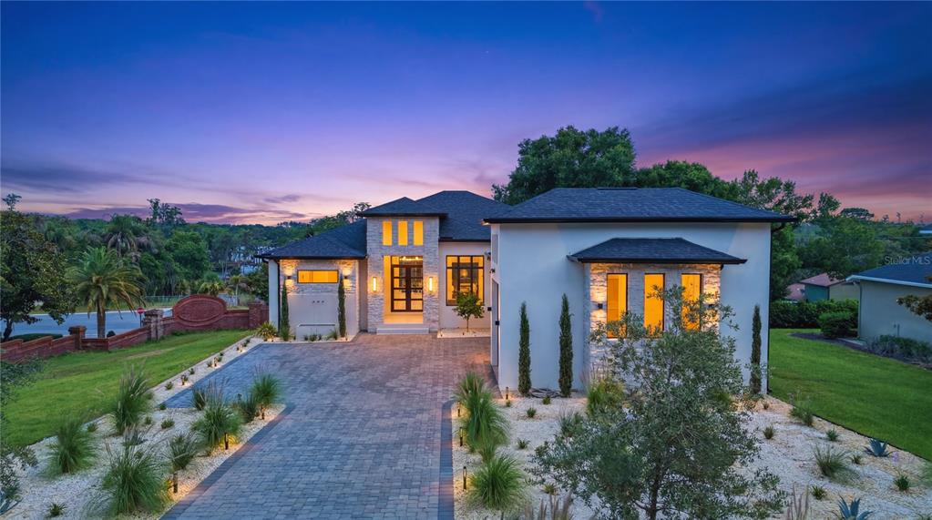 A modern single-story house with a stone facade and a paved driveway at dusk — 11500 OSPREY POINTE BOULEVARD, CLERMONT, FL