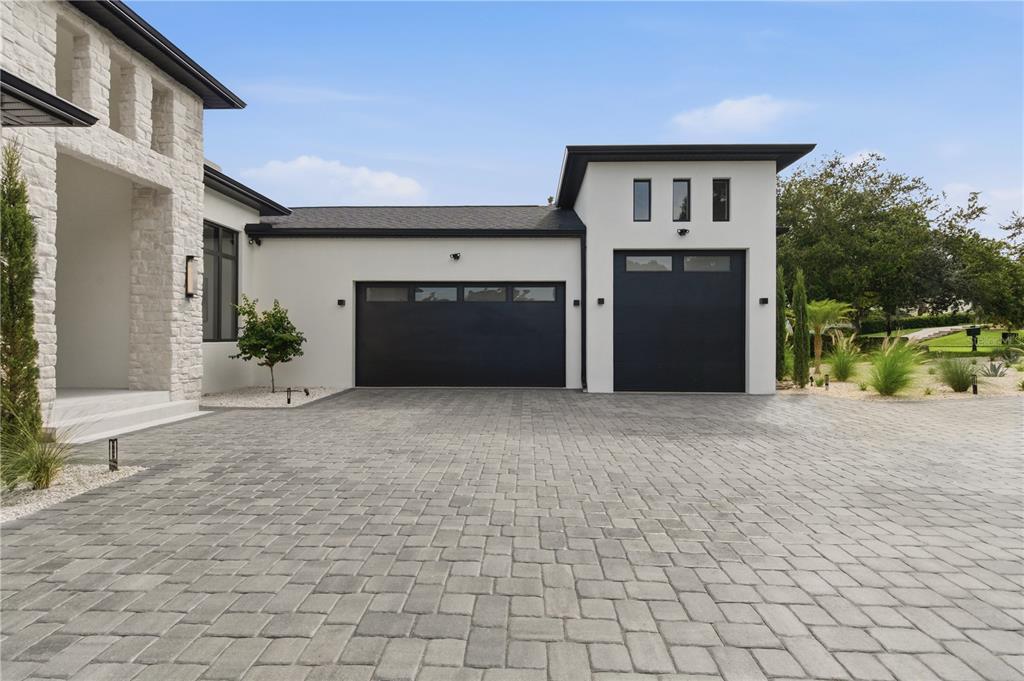 A modern house exterior features a stone facade, white walls, and a paved driveway — 11500 OSPREY POINTE BOULEVARD, CLERMONT, FL
