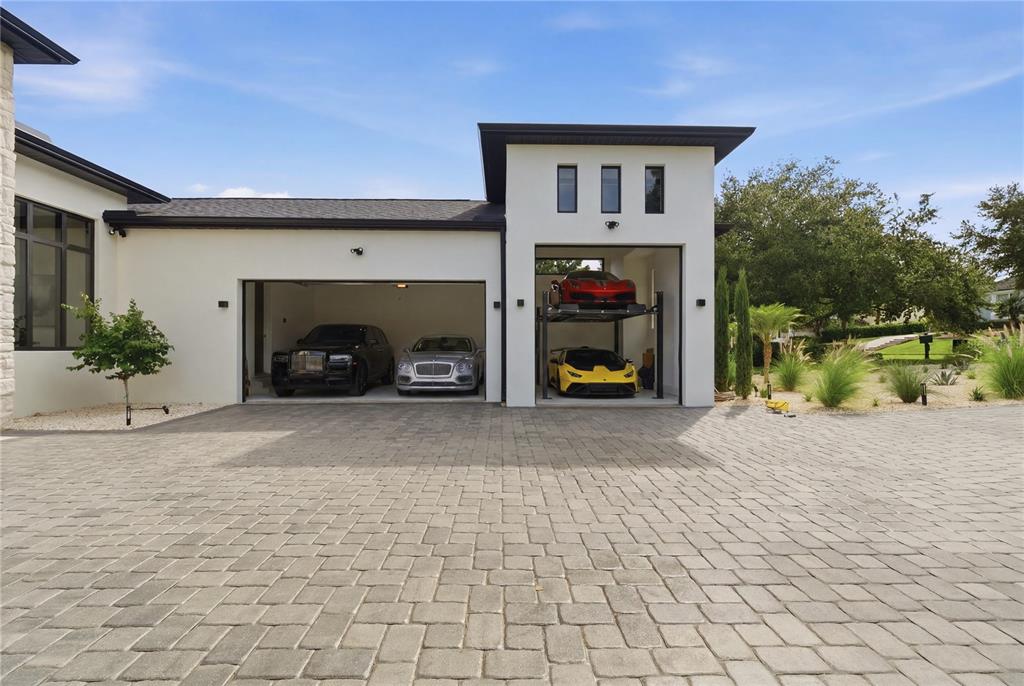 A modern house exterior features a two-car garage and a separate bay with a car lift — 11500 OSPREY POINTE BOULEVARD, CLERMONT, FL