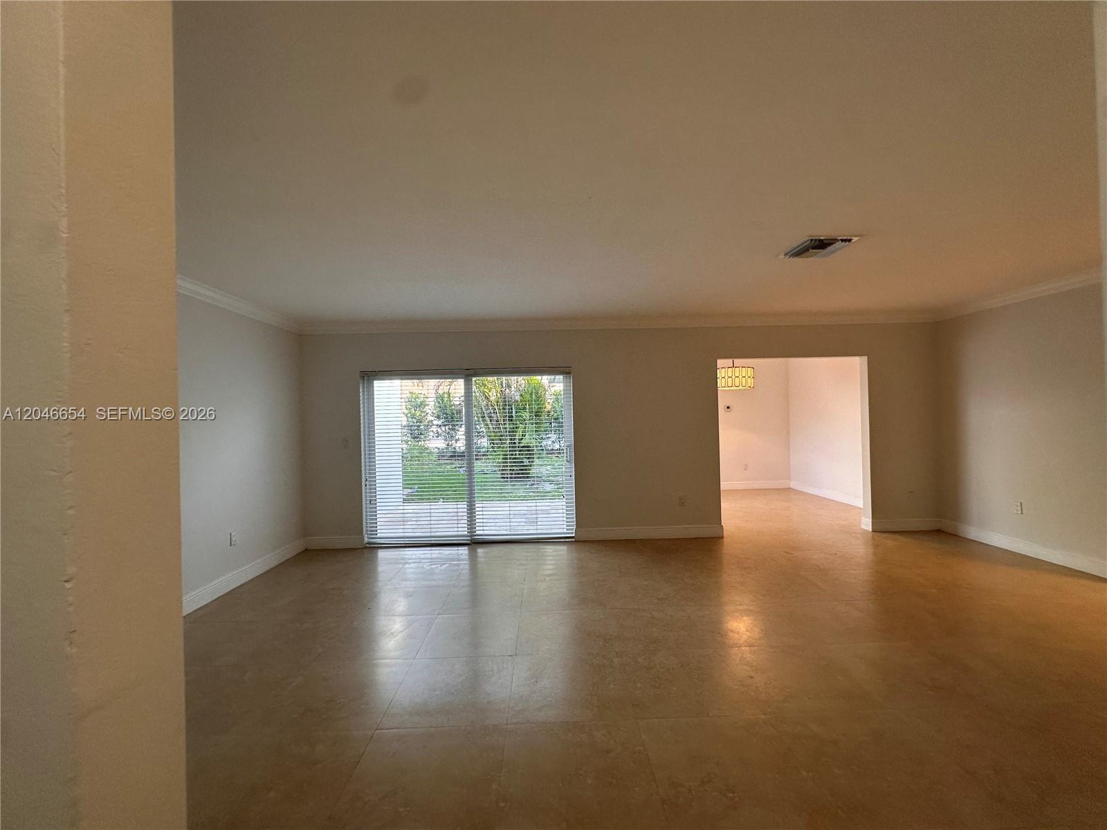 A spacious living room features light-colored tile flooring, neutral walls, and sliding glass patio doors — 1130 Cotorro Ave # 1130, Coral Gables FL 33146, CORAL GABLES, FL