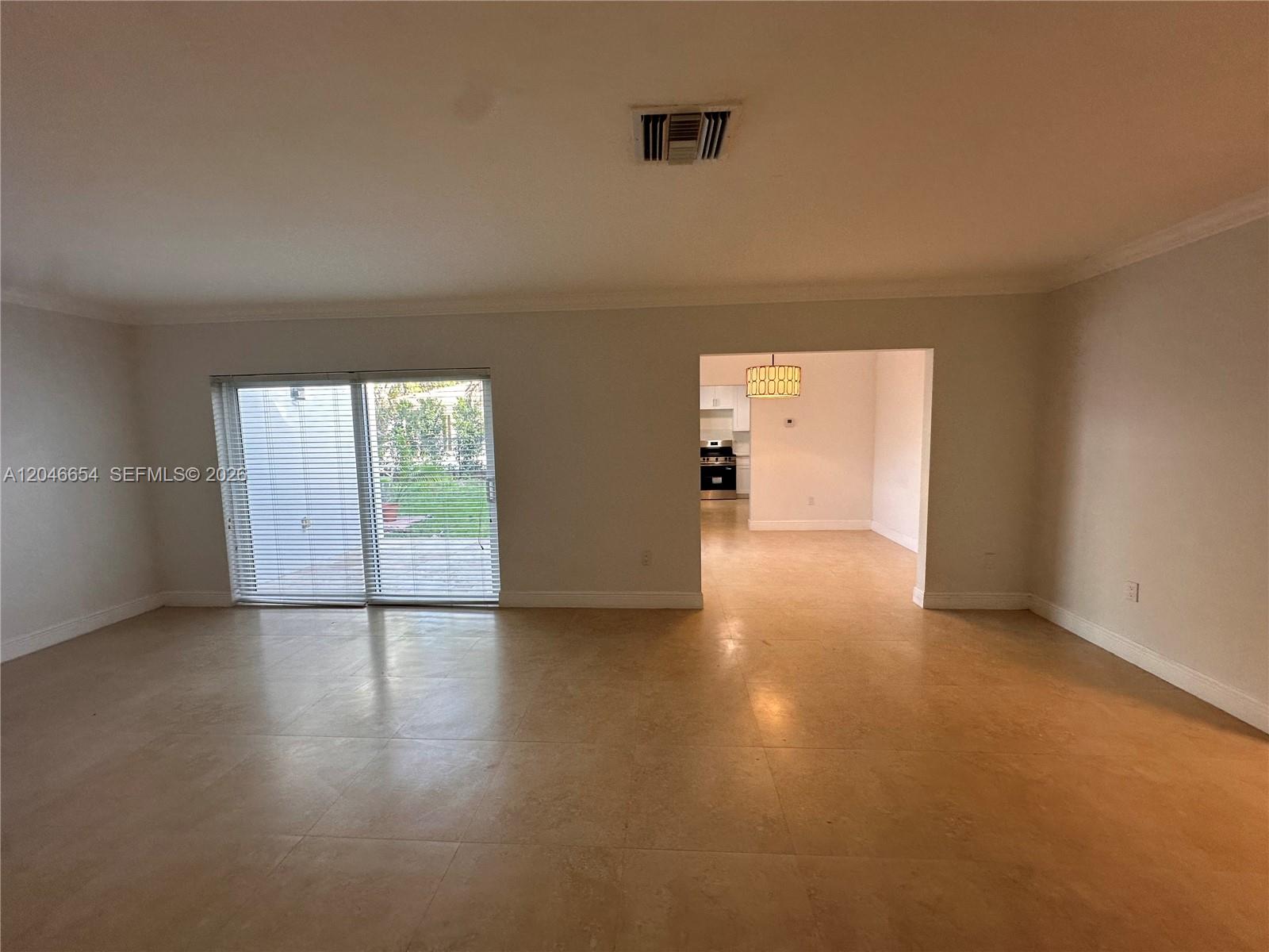 A spacious living room features light-colored tile flooring, a sliding glass door, and an adjacent kitchen — 1130 Cotorro Ave # 1130, Coral Gables FL 33146, CORAL GABLES, FL