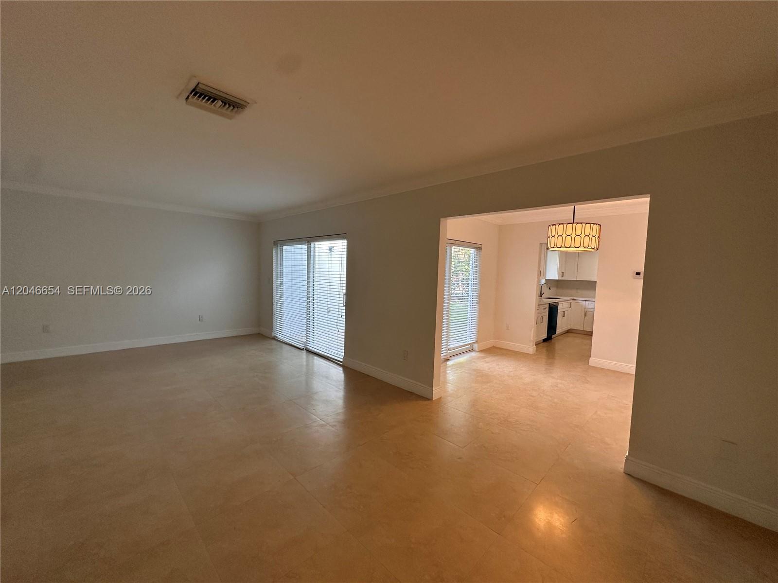 An empty living room with tile flooring leads into a kitchen with a pendant light — 1130 Cotorro Ave # 1130, Coral Gables FL 33146, CORAL GABLES, FL