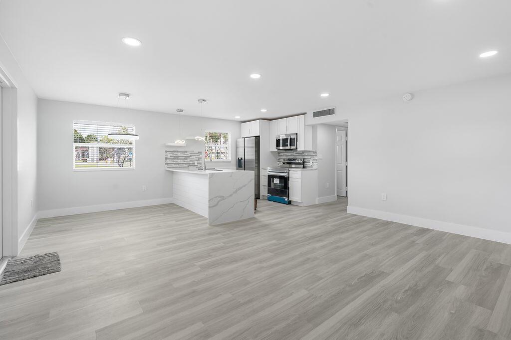 A bright, open-concept kitchen and living area featuring white cabinets, marble-look countertops, and light flooring — 385 Flanders I, Delray Beach FL 33484, DELRAY BEACH, FL