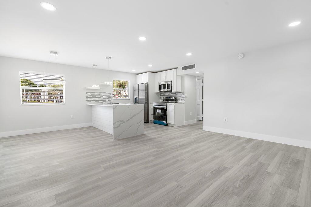 A modern kitchen with white cabinets, marble-patterned island, and light wood-look flooring — 385 Flanders I, Delray Beach FL 33484, DELRAY BEACH, FL