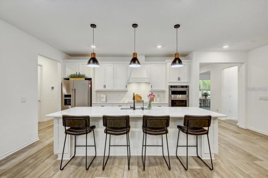 A modern kitchen features a white island with four stools, pendant lighting, and stainless appliances — 2824 QUAIL CREST COURT, VALRICO, FL