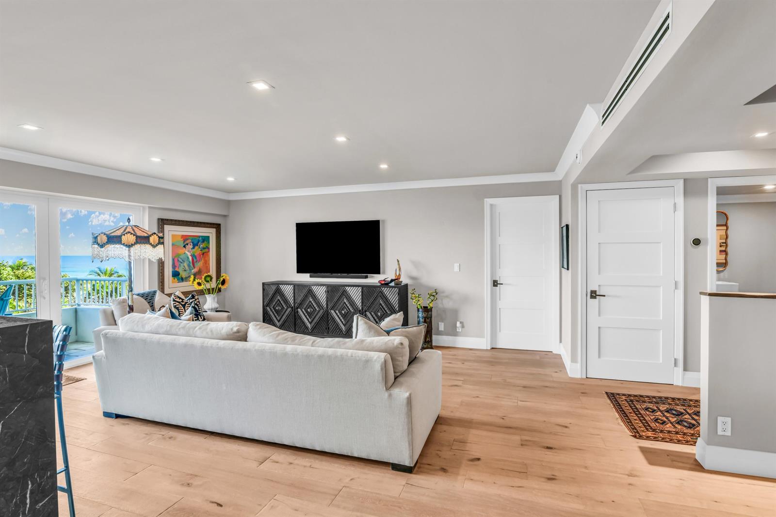 A living room features light wood floors, a white sofa, a television, and a balcony view — 600 S Ocean Boulevard # 407, Boca Raton FL 33432, BOCA RATON, FL