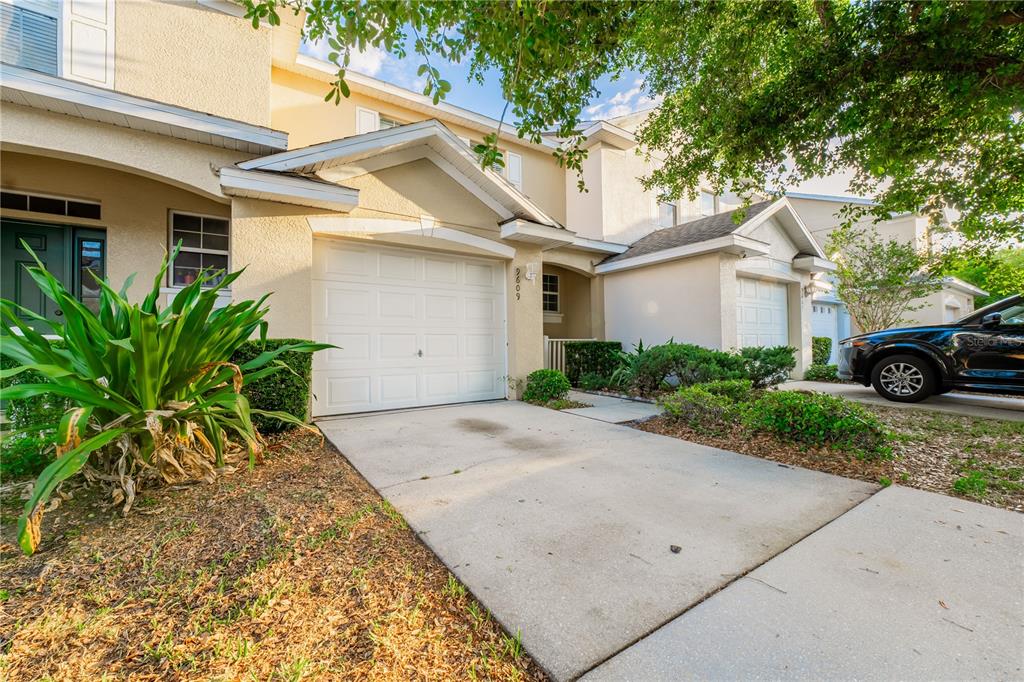 A two-story townhouse exterior features a white garage door, a concrete driveway, and landscaping — 9609 CARLSDALE DRIVE, RIVERVIEW, FL