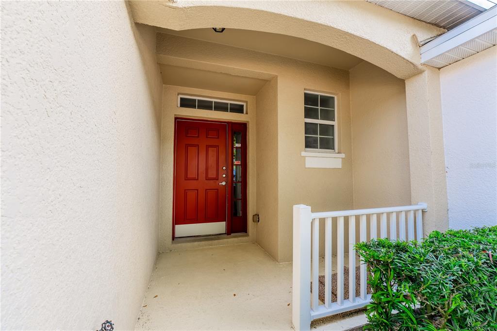 A red front door with a side light and transom window sits under a covered porch — 9609 CARLSDALE DRIVE, RIVERVIEW, FL