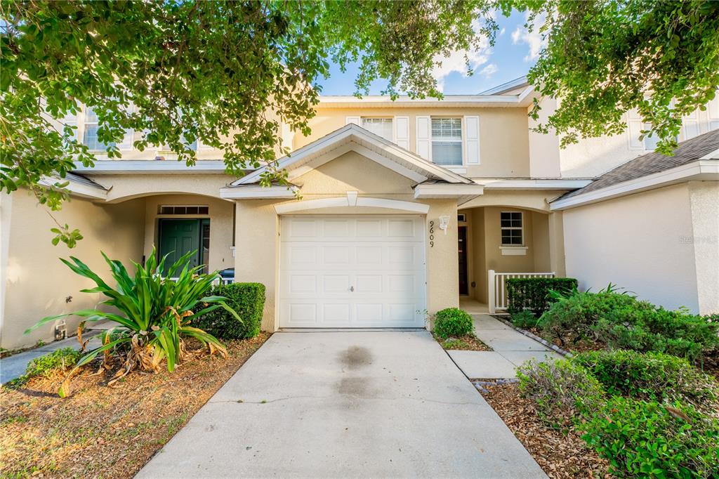 A two-story townhouse exterior features a single-car garage, a concrete driveway, and landscaped front yard — 9609 CARLSDALE DRIVE, RIVERVIEW, FL