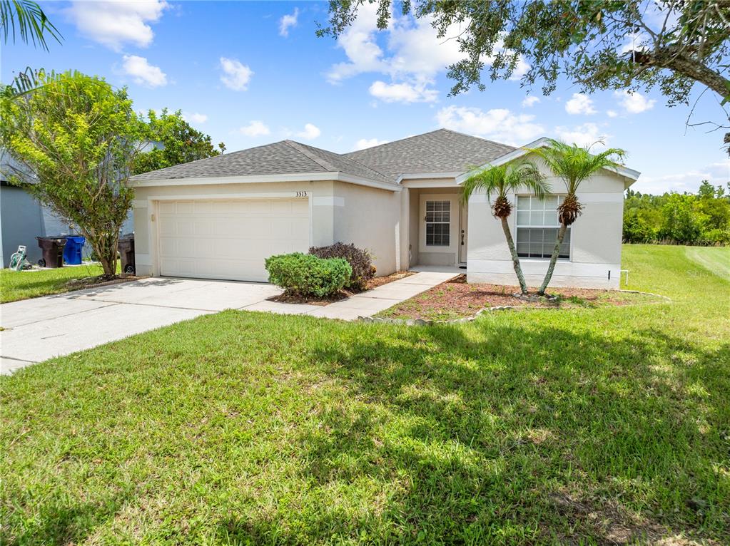 A single-story house with a beige stucco exterior, a two-car garage, and a front lawn — 3313 PEKIN STREET, ST CLOUD, FL