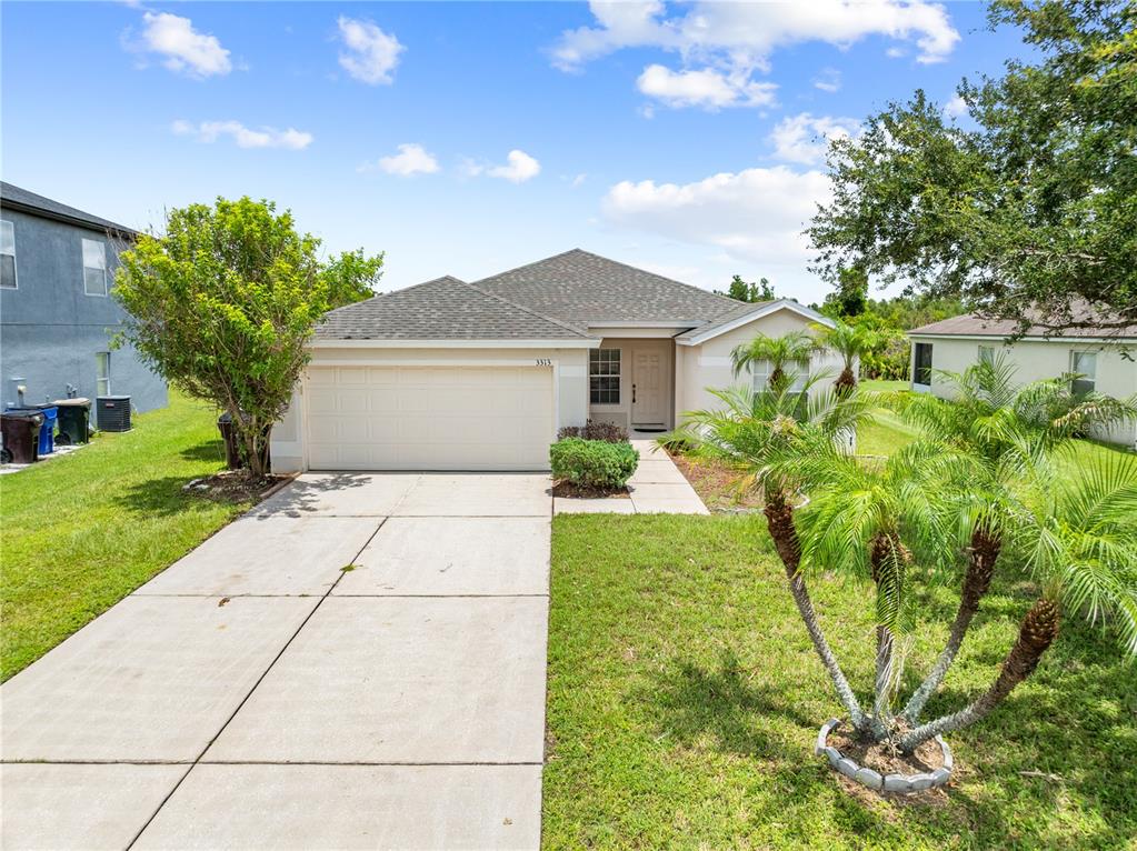 A single-story suburban house with a two-car garage, concrete driveway, and front yard landscaping — 3313 PEKIN STREET, ST CLOUD, FL
