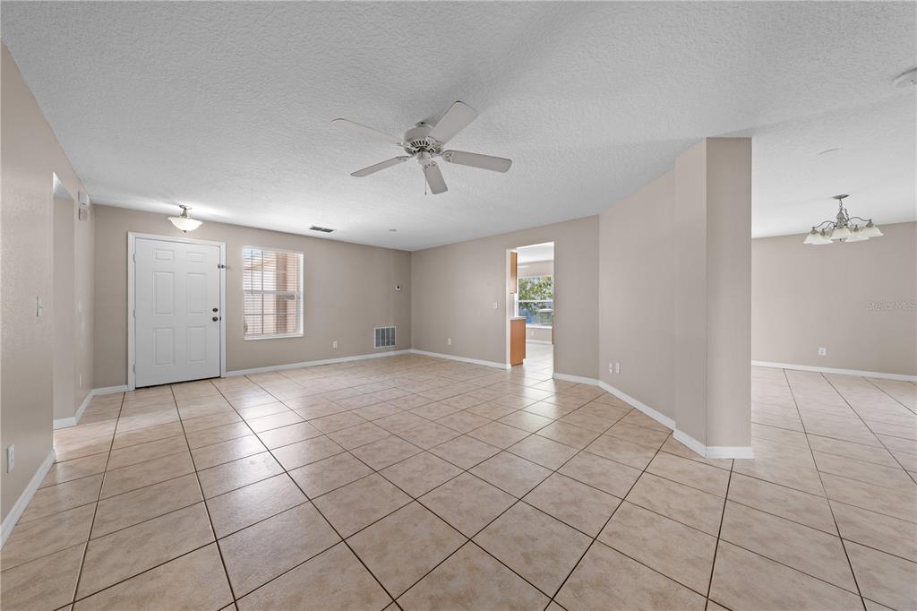 A spacious, empty living room with beige walls, tan tile flooring, and a ceiling fan — 3313 PEKIN STREET, ST CLOUD, FL