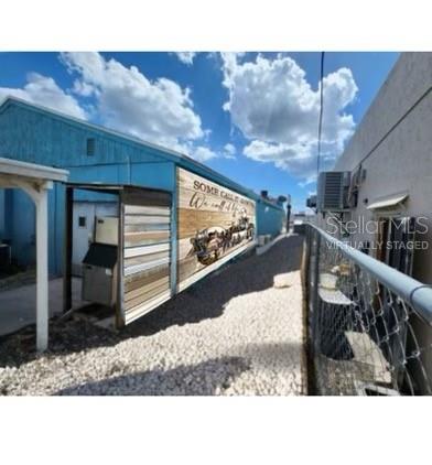 A narrow outdoor walkway runs between a blue building with a mural and a chain-link fence — 3496 TAMIAMI TRAIL, PORT CHARLOTTE, FL