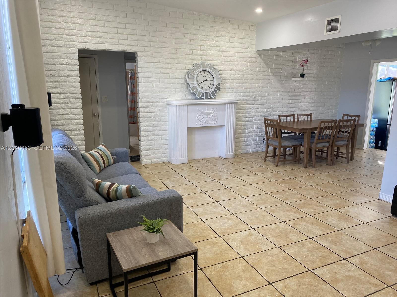A living and dining area features a white brick wall, fireplace, and tiled flooring — 540 NW 111 St, Miami FL 33168, MIAMI, FL