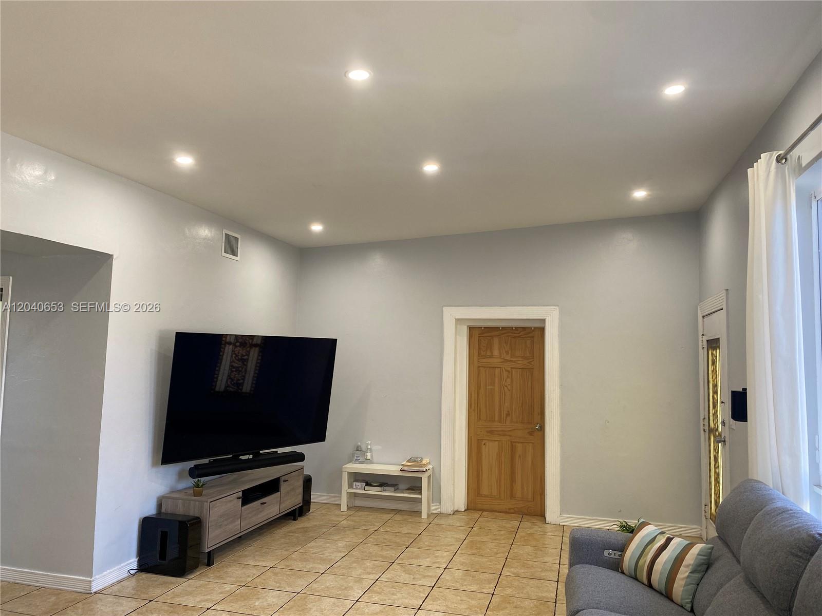 A living room features light gray walls, tile flooring, a wall-mounted television, and a wooden door — 540 NW 111 St, Miami FL 33168, MIAMI, FL