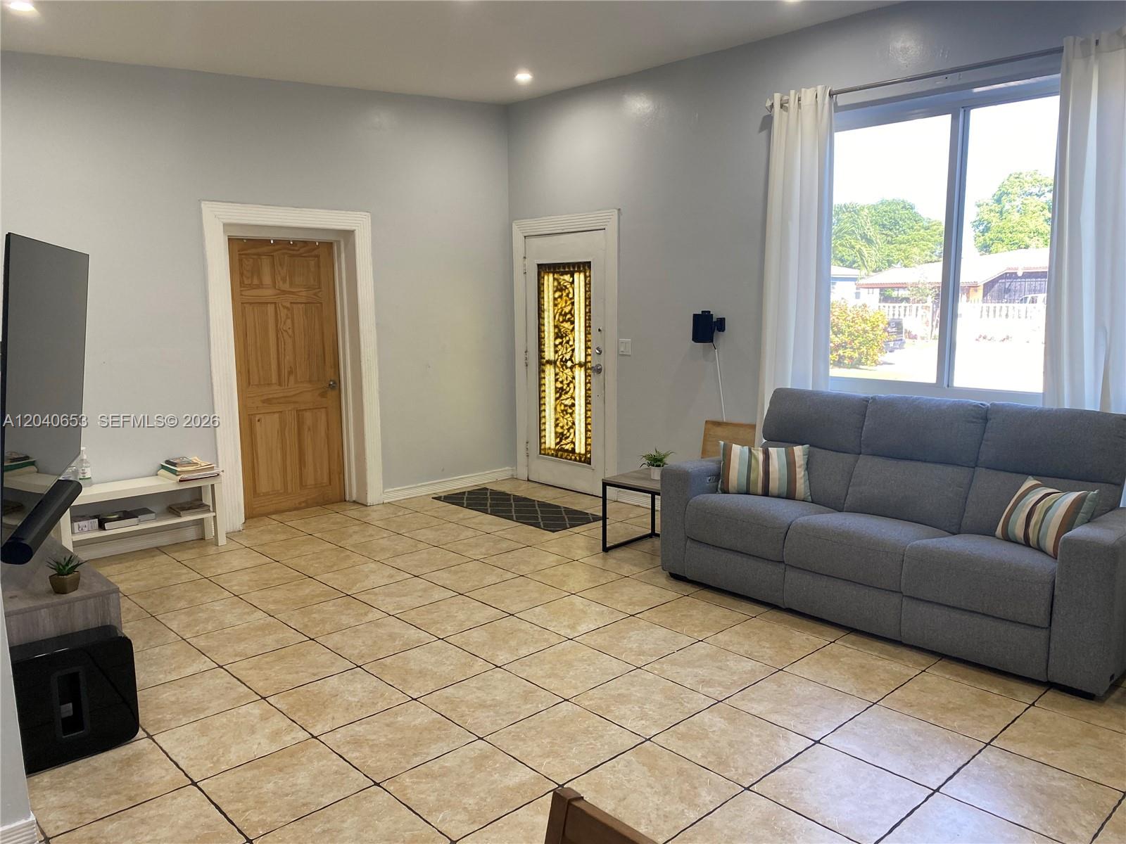 A living room features light-colored tile flooring, a gray sofa, and a front door with glass — 540 NW 111 St, Miami FL 33168, MIAMI, FL