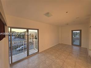 An empty room with light-colored tile flooring, a sliding glass door to a balcony, and windows — 2389 NW 26th St # 2B, Miami FL 33142, MIAMI, FL