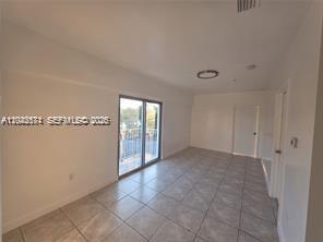 An empty room with light-colored tile flooring, white walls, and a sliding glass balcony door — 2389 NW 26th St # 2B, Miami FL 33142, MIAMI, FL