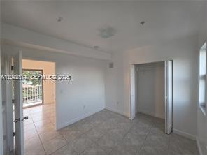 A bedroom with light tile flooring, white walls, a closet, and a doorway to a balcony — 2389 NW 26th St # 2B, Miami FL 33142, MIAMI, FL