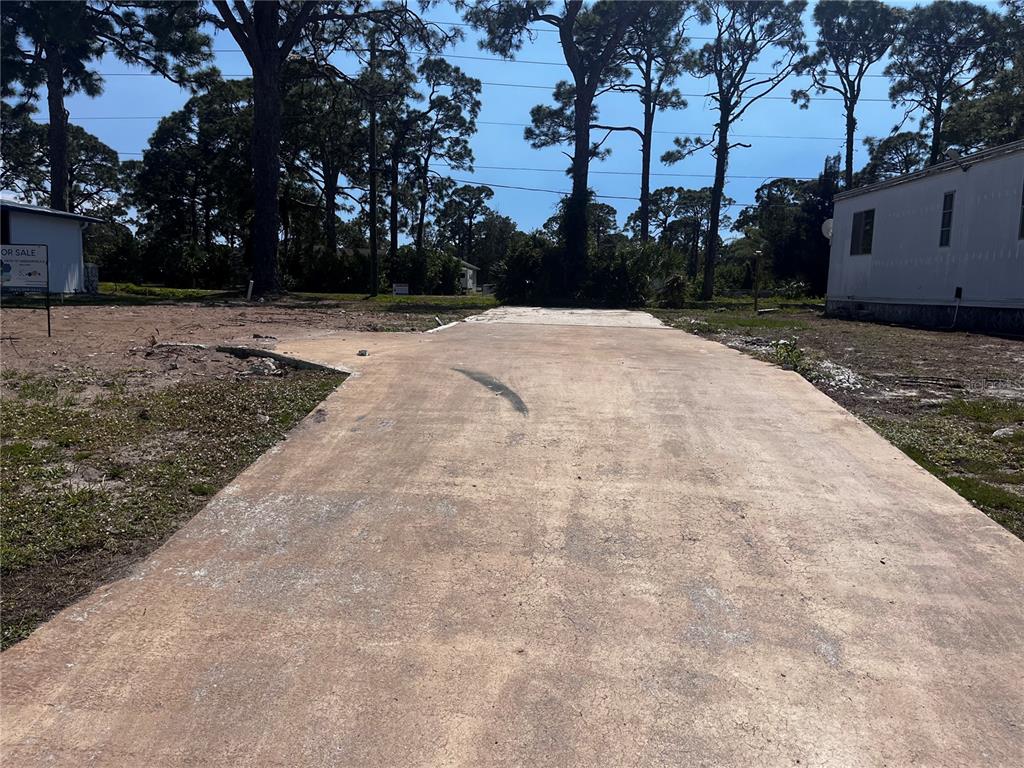 A concrete driveway leads to a vacant lot with trees and a neighboring mobile home — 181 S FIJI CIRCLE UNIT 181, ENGLEWOOD, FL