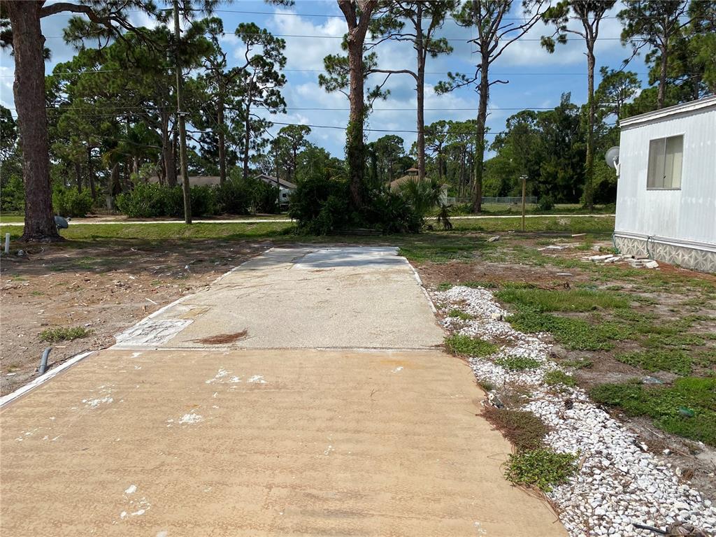 A concrete driveway leads toward a wooded area next to a mobile home — 181 S FIJI CIRCLE UNIT 181, ENGLEWOOD, FL