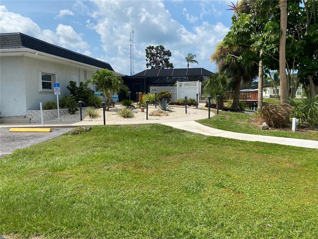 A paved walkway leads past a landscaped garden toward a building with a screened enclosure — 181 S FIJI CIRCLE UNIT 181, ENGLEWOOD, FL