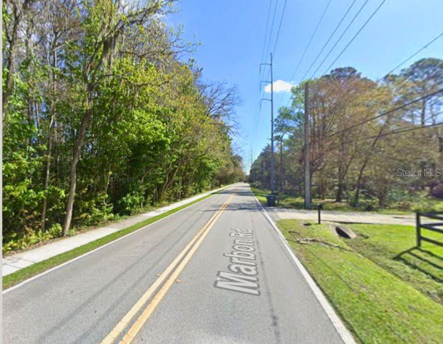 A paved road stretches into the distance, flanked by dense trees and a grassy shoulder — MARBON ROAD, JACKSONVILLE, FL