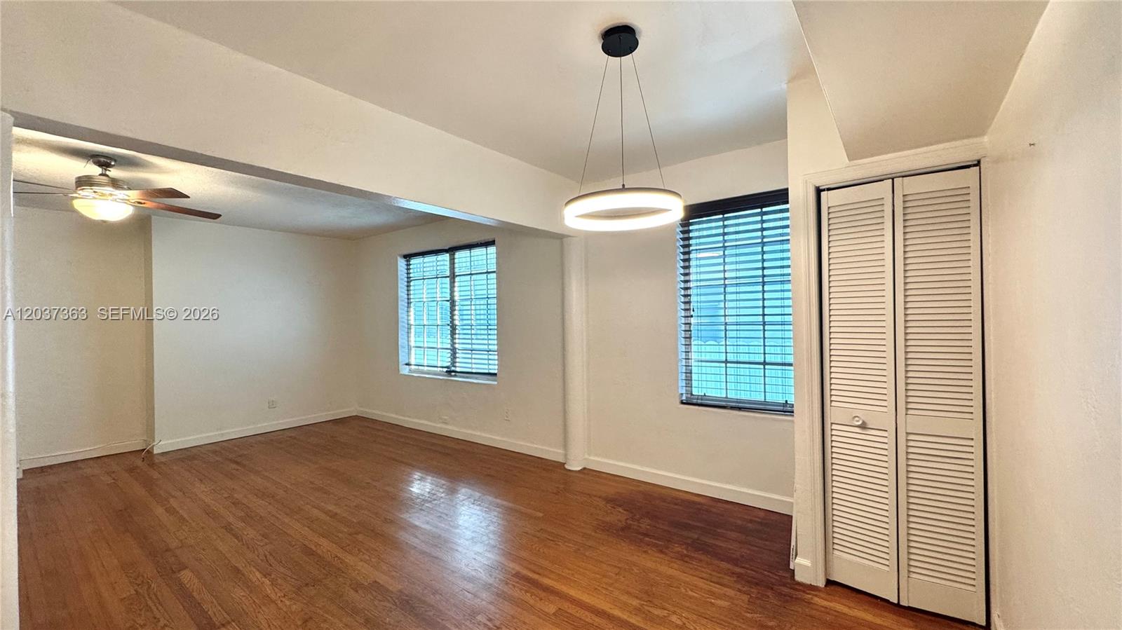 An empty room features hardwood floors, two windows with blinds, and a modern circular light — 751 Euclid Ave # 2, Miami Beach FL 33139, MIAMI BEACH, FL