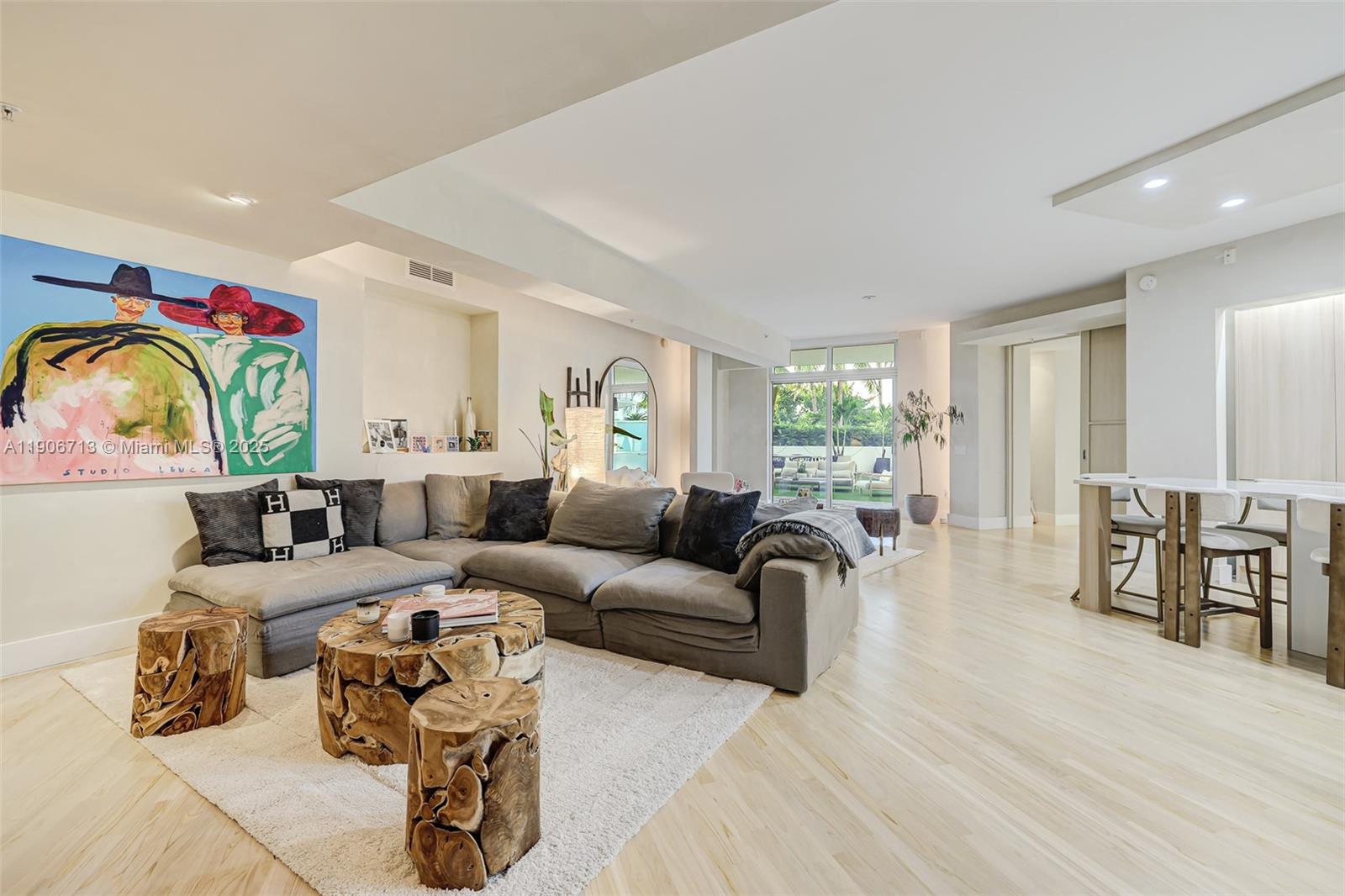 A living room features a large grey sectional, wooden stump tables, and a vibrant wall painting — 2001 Meridian Ave # 307, Miami Beach FL 33139, MIAMI BEACH, FL