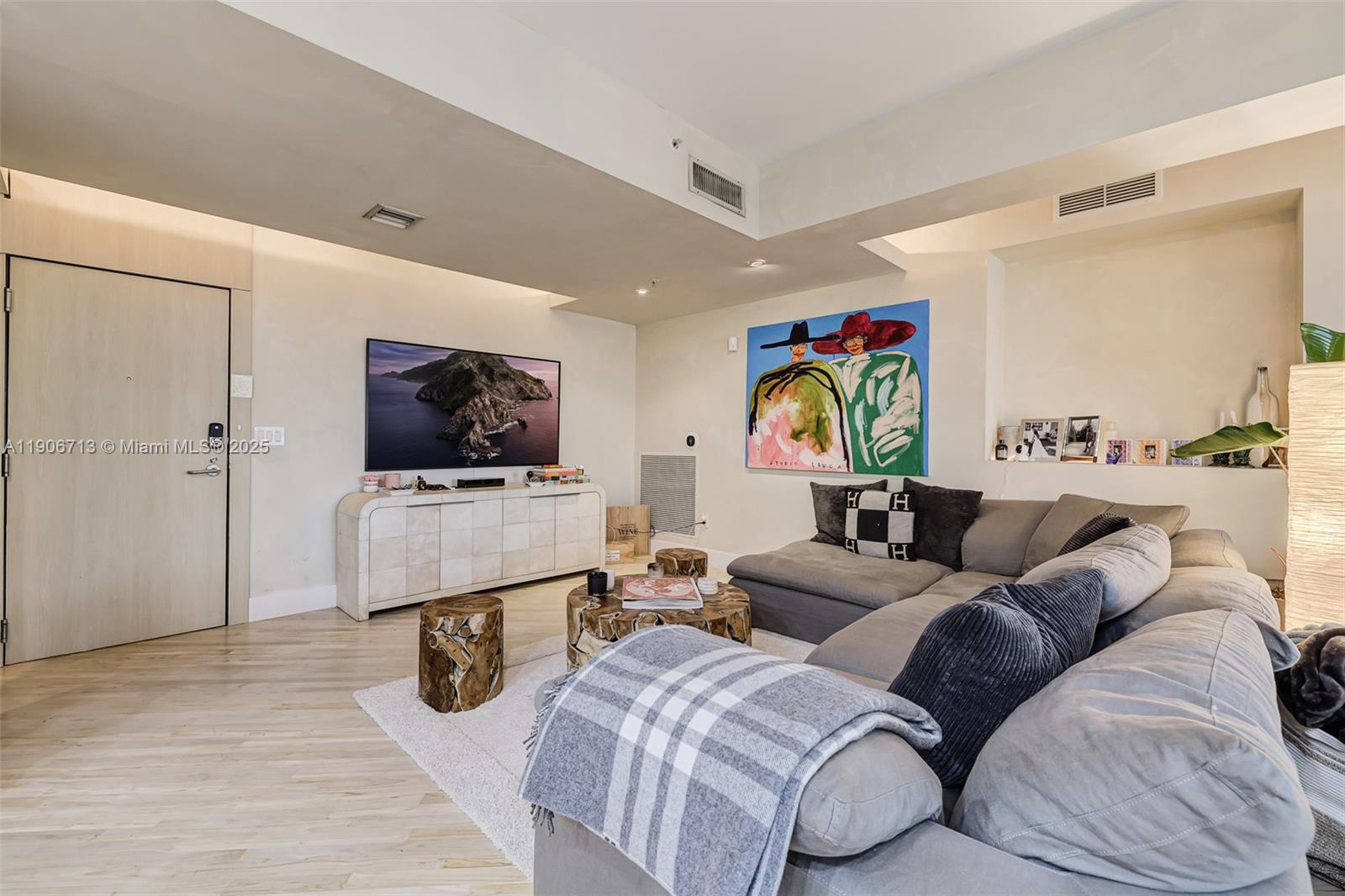A living room features a grey sectional sofa, a television, and light wood flooring — 2001 Meridian Ave # 307, Miami Beach FL 33139, MIAMI BEACH, FL