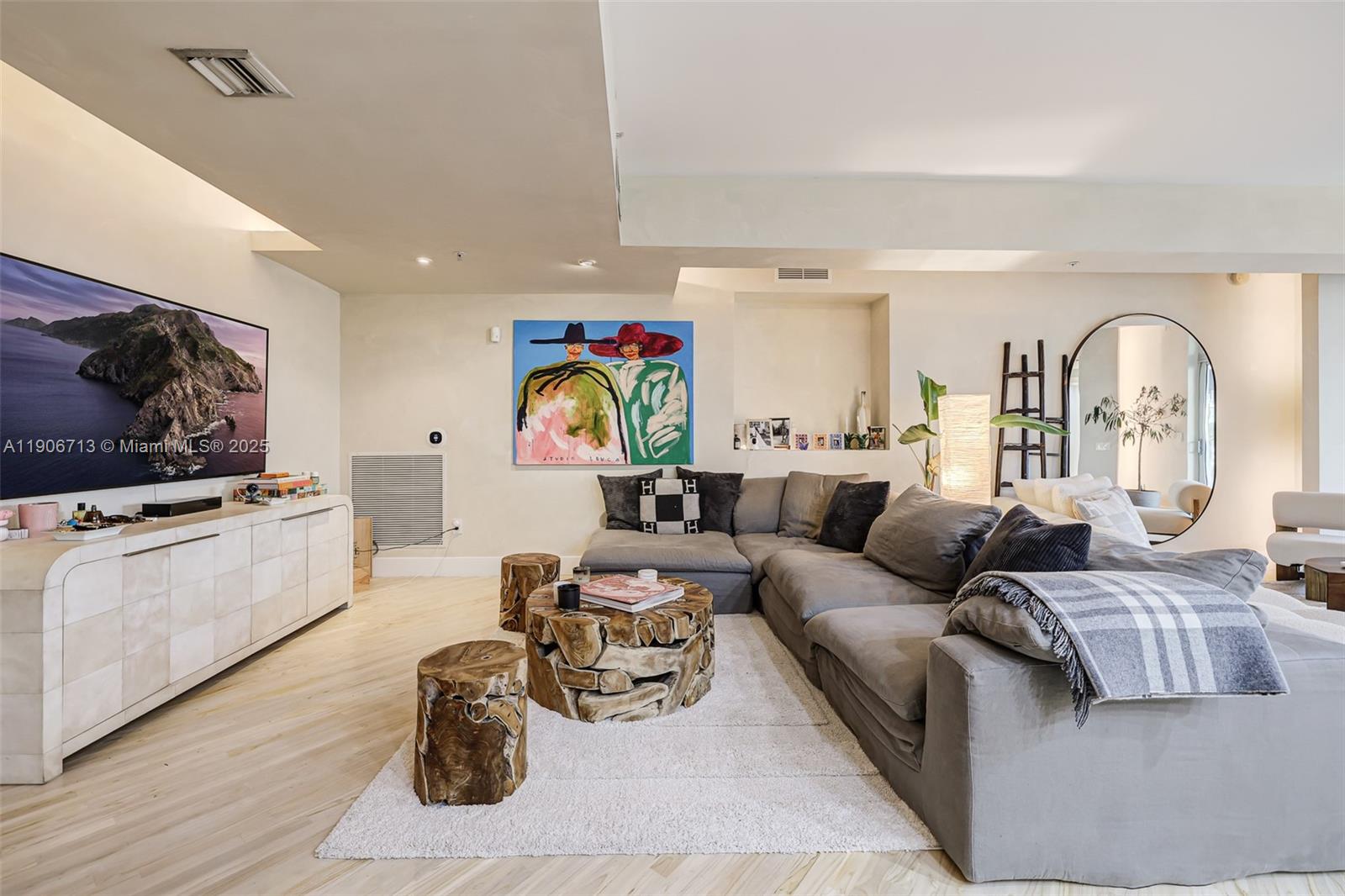 A living room features a large gray sectional sofa, wooden stump tables, and a television — 2001 Meridian Ave # 307, Miami Beach FL 33139, MIAMI BEACH, FL